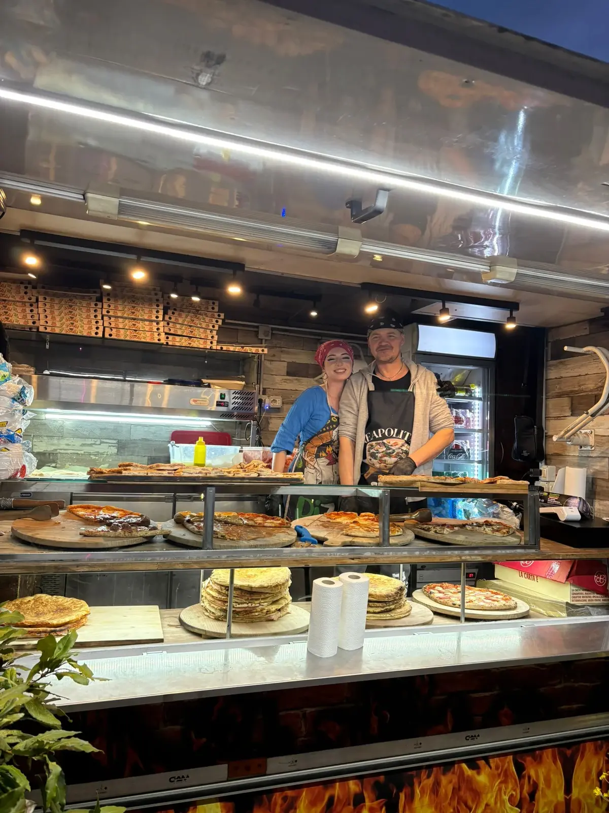 Due pizzaioli dietro al banco carico di pizze e schiacciate