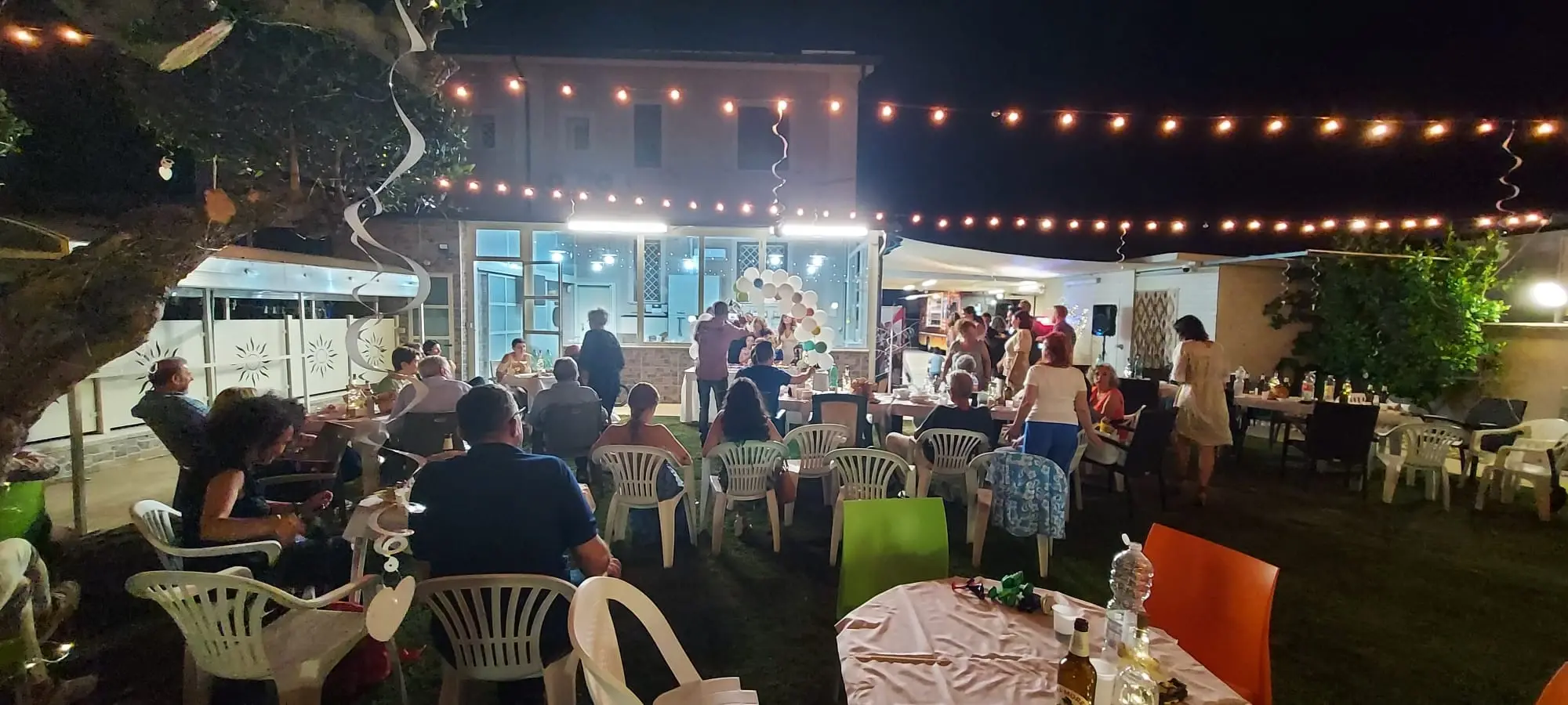 Tavolate sotto le luminarie accese, di sera, in un giardino