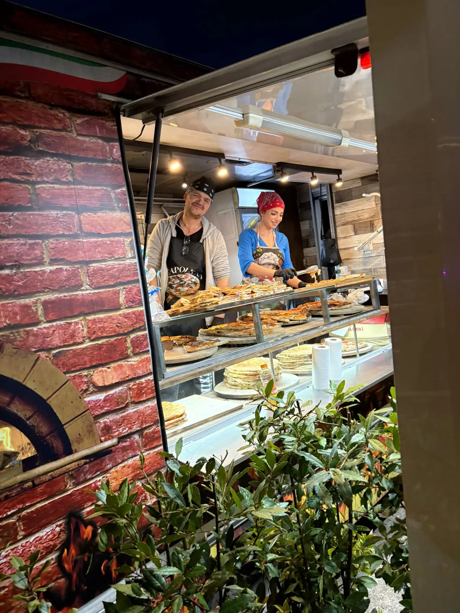 Il banco del camion aperto di sera, con i due pizzaioli e le schiacciate in mostra